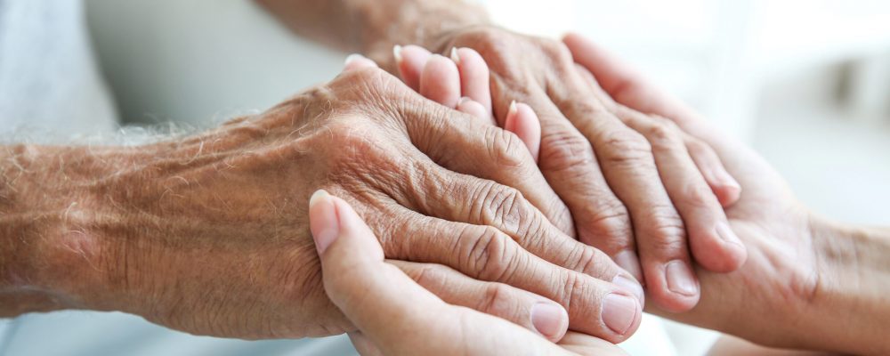 junge Frauenhände halten die Hände eines Seniors/älteren Herrn (Nahaufnahme)