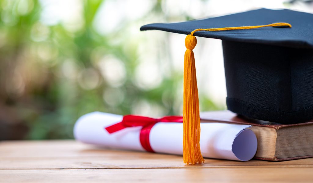 A black graduation cap and a certificate placed on an old book